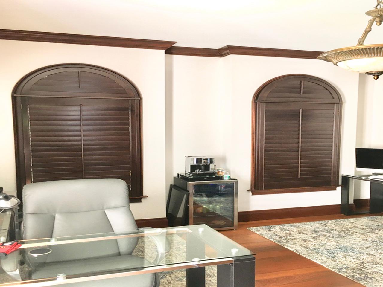Home office with stained arched shutters with louvers closed